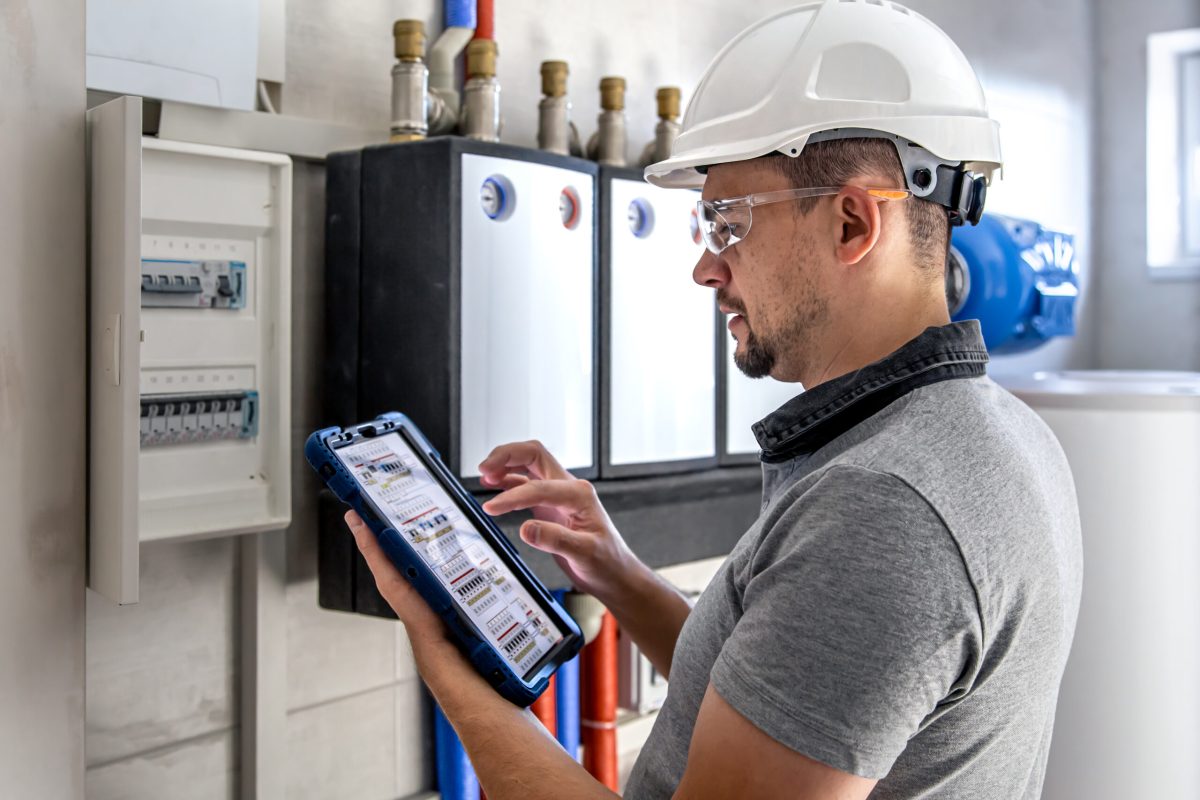 Man, an electrical technician working in a switchboard with fuses. Installation and connection of electrical equipment. Professional uses a tablet.