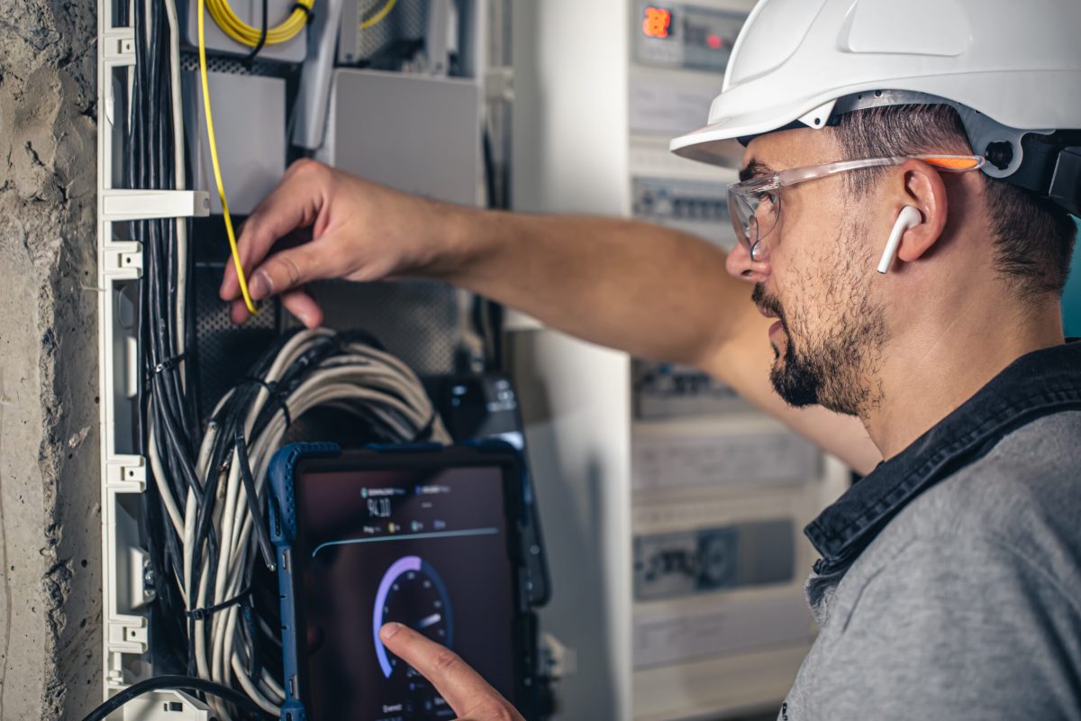 Man, an electrical technician working in a switchboard with fuses. Installation and connection of electrical equipment. Professional uses a tablet.
